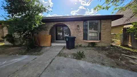 Front of a tan brick home with bare dirt and a trash bin before the landscaping