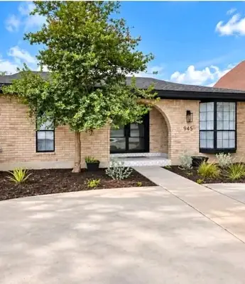 Front yard of a tan brick home with new planted beds