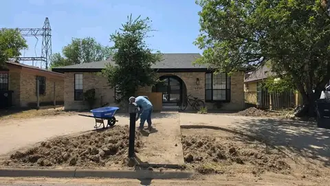 A worker beside a wheelbarrow, working the soil in the front yard
